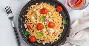 Spaghetti-with-baked-feta-cherry-tomatoes-herbs-basil-gray-background-top-view-horizontal