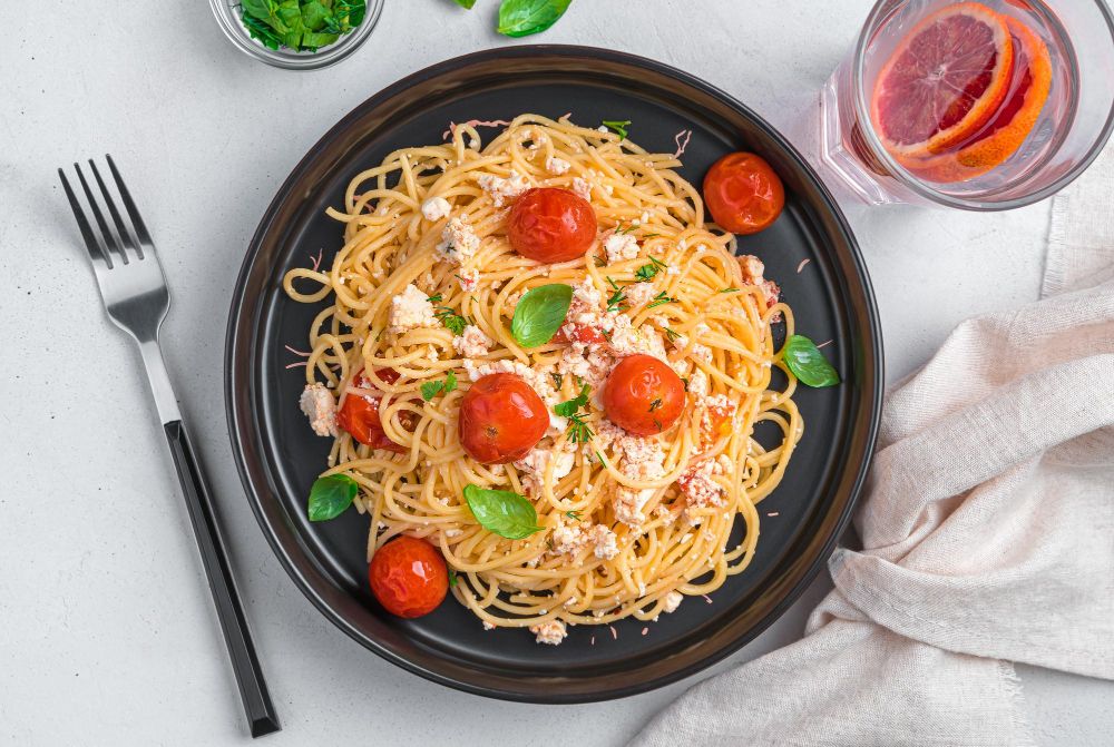 Spaghetti-with-baked-feta-cherry-tomatoes-herbs-basil-gray-background-top-view-horizontal